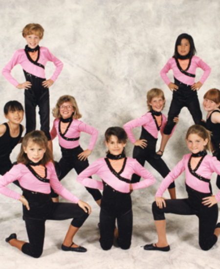 A group of young dancers in coordinated pink and black outfits pose confidently.