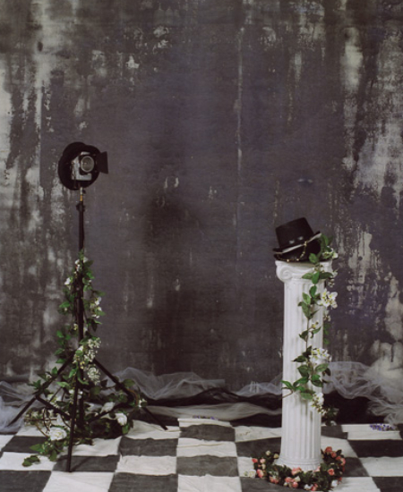 Vintage microphone on stand with floral decorations beside a white pedestal and top hat.