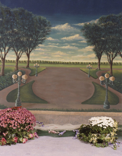 A serene park pathway flanked by trees and lampposts under a partly cloudy sky.