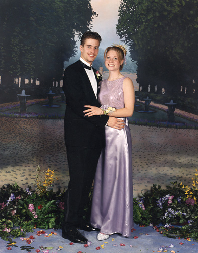 A couple dressed formally, posing together outdoors at night.