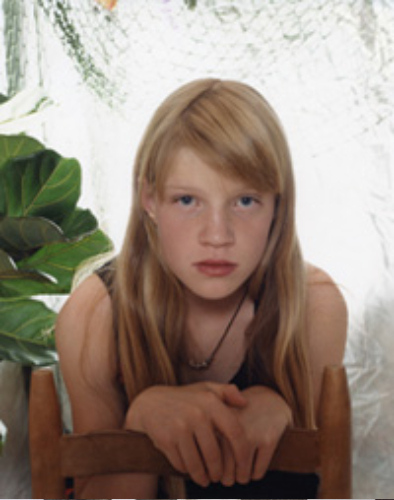 Portrait of a young girl with blonde hair and blue eyes indoors.