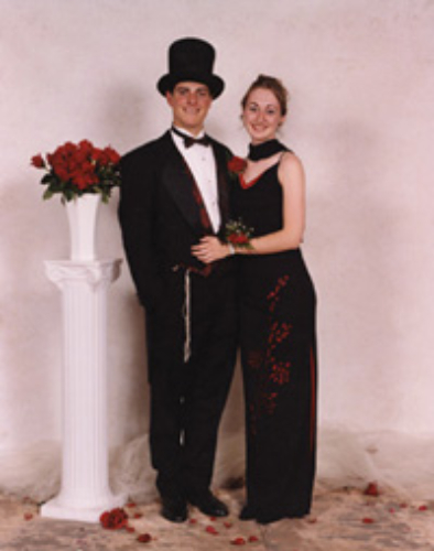 Couple dressed elegantly, posing with a bouquet of red roses.