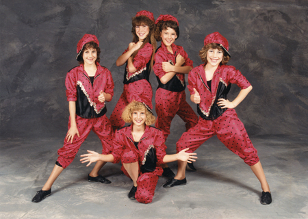 A group of six performers in coordinated red costumes striking playful poses.