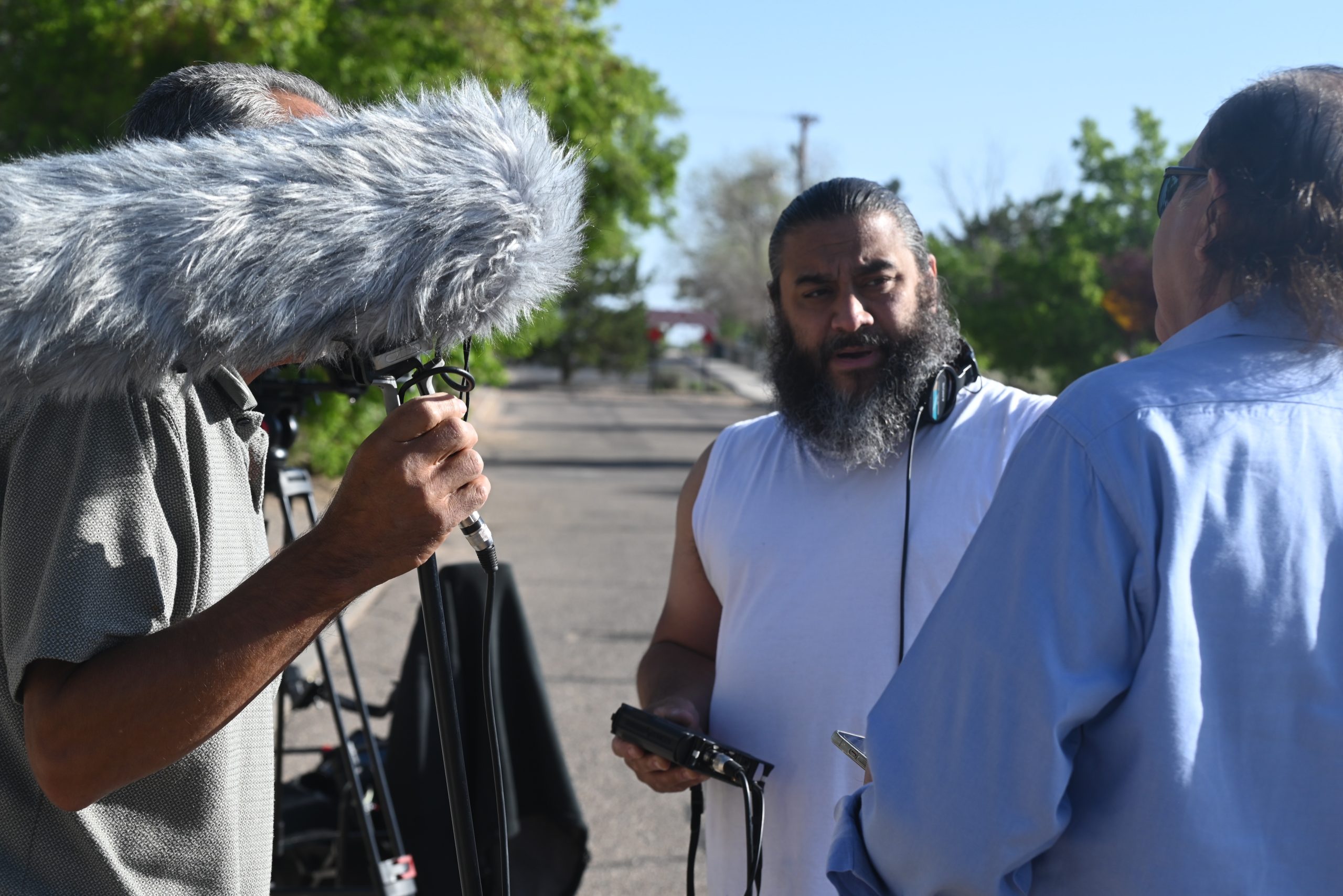 Man with a beard and white tank top being interviewed outdoors.
