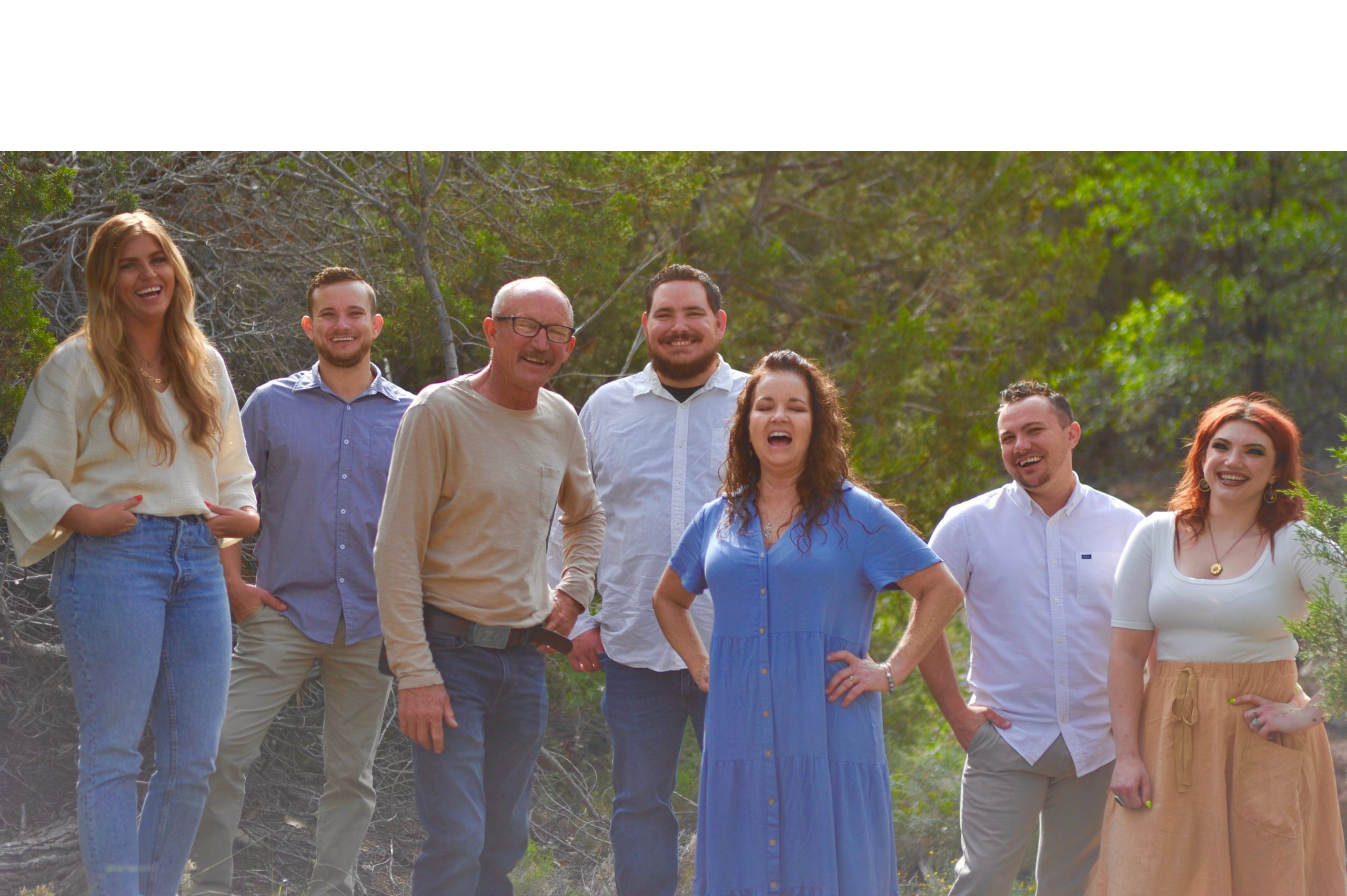 A joyful group of five people posing outdoors in casual attire.