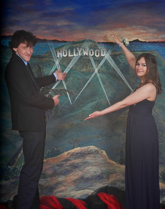 A man and woman in formal wear celebrating with champagne in front of a Hollywood mural.