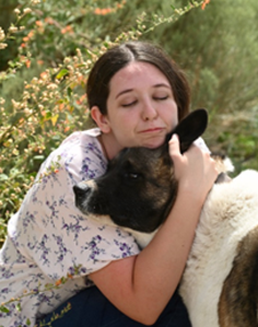 A woman lovingly hugging a black-faced sheep outdoors.
