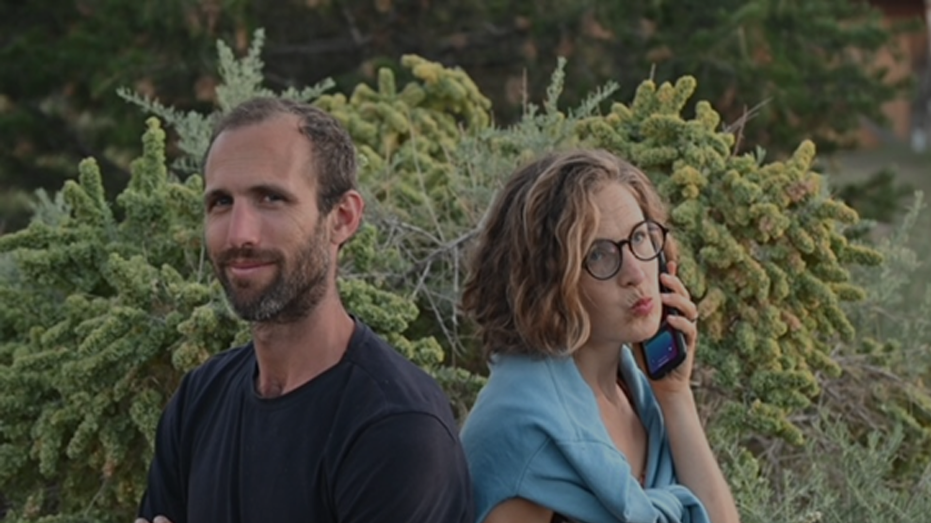 Man and woman standing back-to-back outdoors, woman on phone.