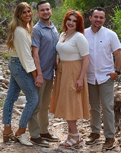 Group of four friends posing outdoors in casual attire.