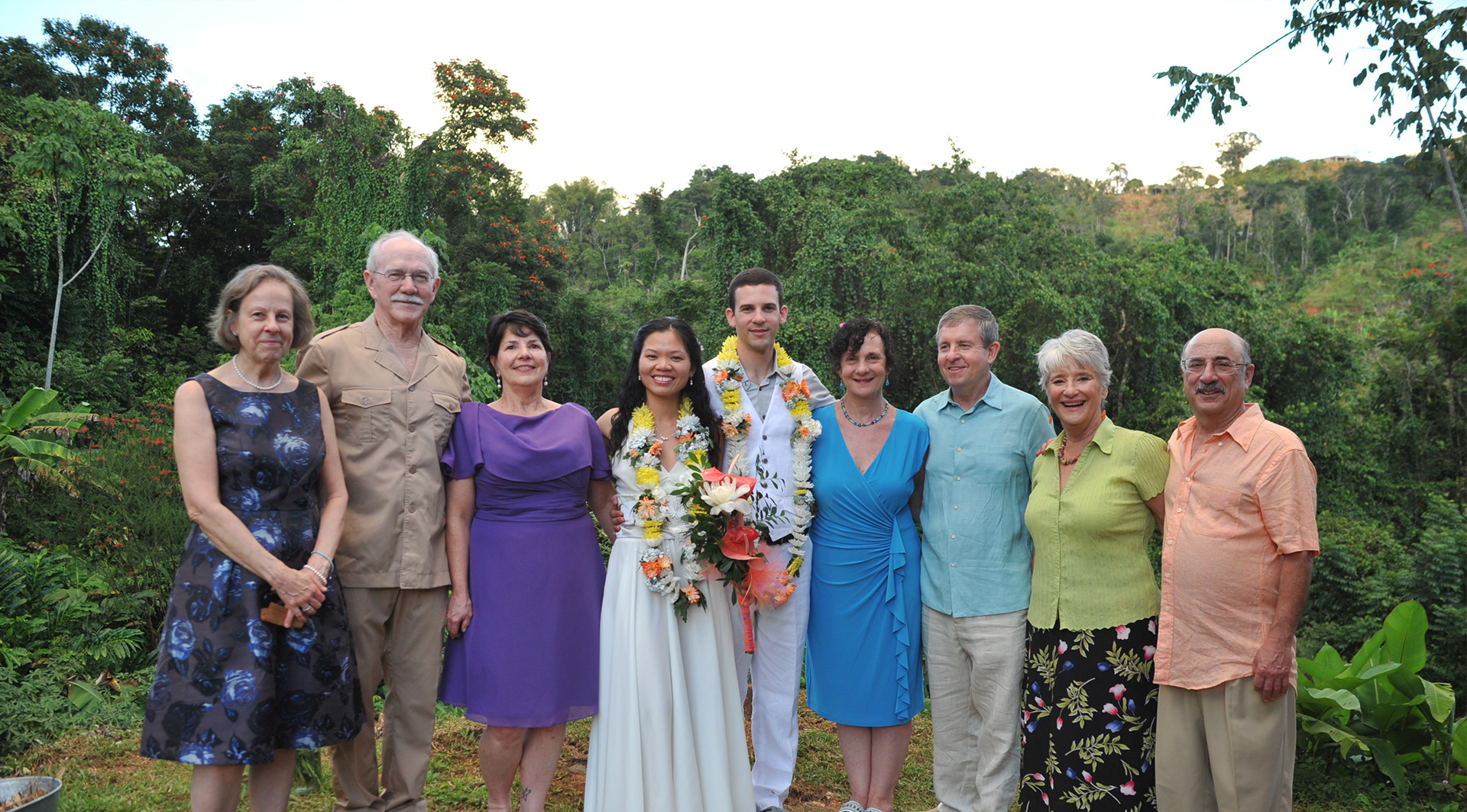 A group of eight people smiling outdoors with trees in the background.