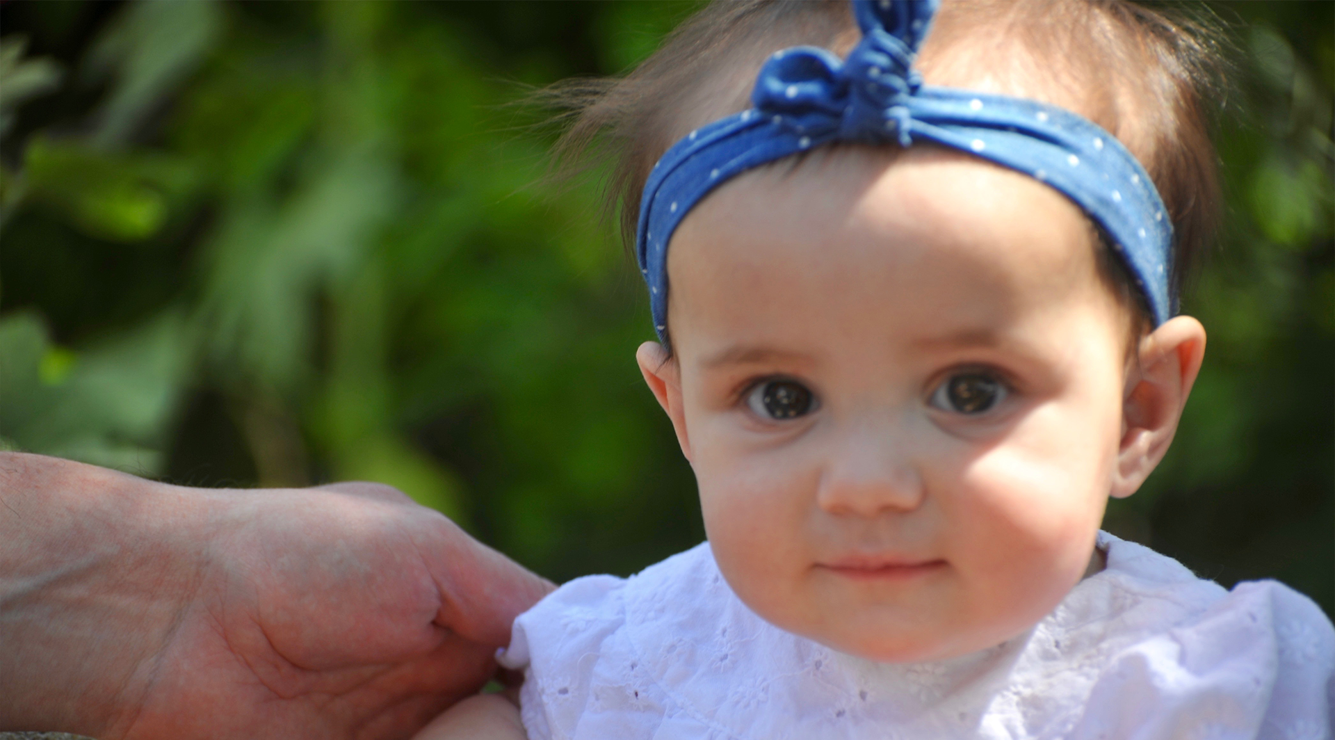 Close-up of a baby girl with a blue headband and curious expression.