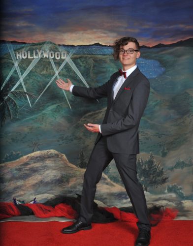 Man in suit posing playfully in front of a Hollywood backdrop.